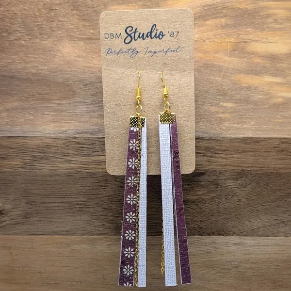 Long, thin rectangle scrapbook paper earrings with layered felt core and mod podge finish. Front: maroon/off-white daisies; back: textured white/purple. Gold chain dangles and metal accents. 